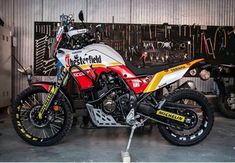 a red, white and yellow motorcycle parked in front of a wall with tools on it