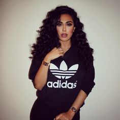 a woman with long black hair wearing a adidas shirt and holding her hand on her hip