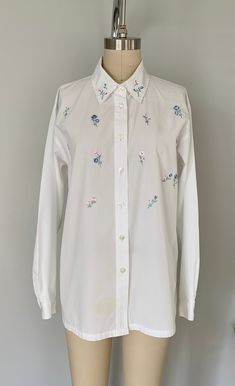 "vintage floral embroidered shirt lovely pastel tone White button down Long sleeves Scalloped collar tag: Napa valley fabric: cotton polyester blend size:Small measurements: shoulder to shoulder 18\" armpit to armpit:21.5\" arm length:22\" total length:27\" condition: good, has some faint spots near sleeve and front bottom" Collared Shirt With Buttons For Spring, Feminine Spring Shirt With Spread Collar, Feminine Spread Collar Shirt For Spring, Elegant Cotton Shirt With Floral Embroidery, Floral Embroidered Cotton Shirt For Work, Cotton Shirt With Floral Embroidery For Work, Feminine Embroidered Cotton Blouse, Classic Embroidered Button-up Shirt, Feminine Cotton Shirt With Button Closure