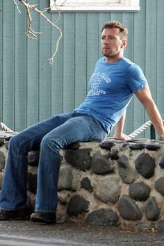 a man sitting on a stone wall with his feet propped up against the rock and looking off into the distance