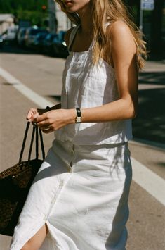 a woman is walking down the street with her hand in her pocket and wearing a white dress