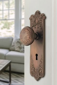 an ornate door handle on the side of a white wall with a couch in the background