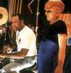 two men sitting next to each other in front of a microphone and an alien head