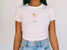 Martini Baby Tee   Women's T-Shirt | Girly Aesthetic | Y2K Trendy Shirt 🌟SHIRT This is a Bella+Canvas baby tee - the material is very soft and very high quality. 🌟SIZING Please find the size chart in listing photo before purchasing. We recommended measuring a t-shirt you already own to get the best fitting t-shirt. 💖CARE/ WASH Machine wash: warm (max 40C or 105F); Non-chlorine: bleach as needed Tumble dry: medium heat; Iron, steam or dry: low heat; Do not dry clean. ✨SHIPPING Your items usually will ship in 2-7 business days. Products shipped from US.  Thanks for shopping small.  Please let me know if you need any custom designs or bulk orders that is not listed, I'll happily custom-make it for you! ♡ Pink Fitted Graphic Tee, Cute Fitted Summer T-shirt, Fitted Graphic Tee With Funny Print, Cute Fitted Shirt With Graphic Print, Fitted Cute Shirt With Graphic Print, Fitted Shirt With Graphic Print In Cute Style, Fitted Pink Graphic Tee Shirt, Cute Fitted White T-shirt, Cute Fitted Cotton Shirt