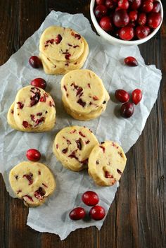 some cranberry cookies are on a piece of paper next to a bowl of cherries