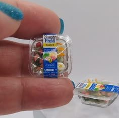 a hand holding a small plastic container with fruit inside