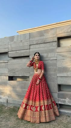 a woman in a red and gold lehenga leaning against a wall with her hand on her hip