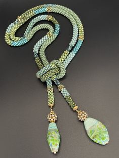 a long beaded necklace with green and blue beads on a black surface, featuring two pendants