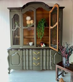 an old china cabinet painted green and decorated with pumpkins, gourds and greenery