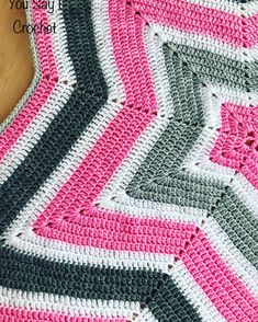 a crocheted blanket is shown with pink, grey and white stripes on it