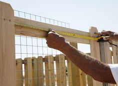 a man measuring the height of a wooden fence with a tape on it's side