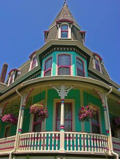 a large green and white house with flowers on the balconies, in front of a blue sky