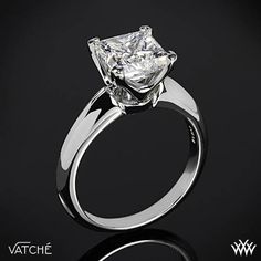 a white gold ring with a princess cut diamond in the center on a black background