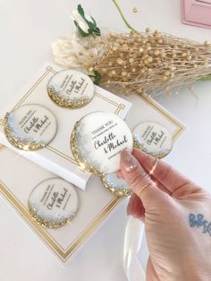 someone is holding up some white and gold wedding cookies with the names of their guests on them