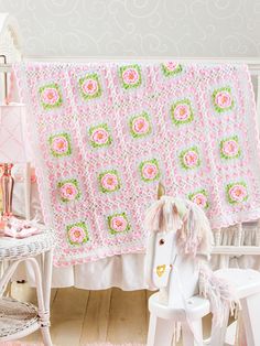 a pink crocheted blanket with a white horse on it and a chair in the background