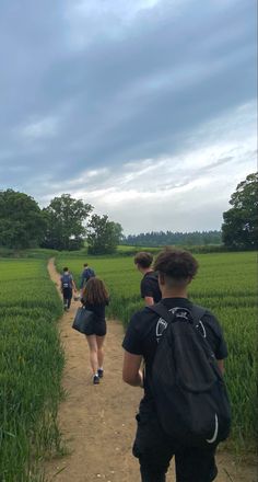 several people walking down a dirt path in the middle of a field