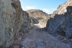 a narrow dirt road between two large rocks on both sides with mountains in the background