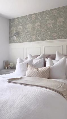 a bed with white linens and pillows in a room that has wallpaper on the walls