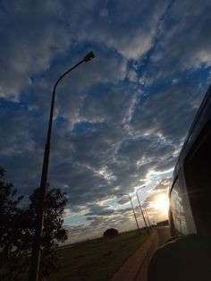 the sun is setting behind some clouds and a street light in front of a bus