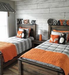 two twin beds with orange and gray bedding in a room that has wood planks on the walls