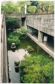 an old concrete building sitting next to a small pond