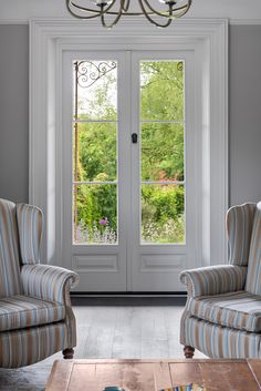 a living room with two chairs and a table in front of the door that leads to another room