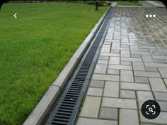 a manhole drain in the middle of a brick walkway next to a green lawn