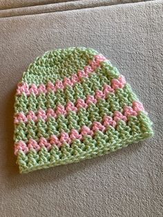 a crocheted green and pink hat laying on top of a white couch next to a wall