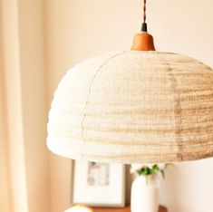 a lamp hanging over a table next to a vase with an apple on it and another fruit in the background