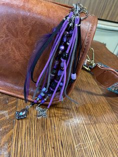 a brown purse with purple and blue tassels sitting on top of a wooden table