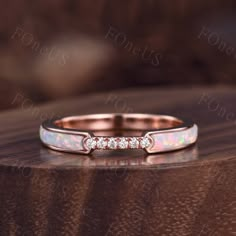 a white opal and diamond ring sitting on top of a wooden table