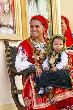 a woman holding a baby in her lap while sitting on a bench with other people