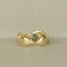 a gold ring with a green stone in the center on a white surface, close up