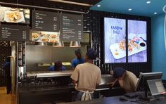 two men working behind the counter at a fast food restaurant with menus on the wall