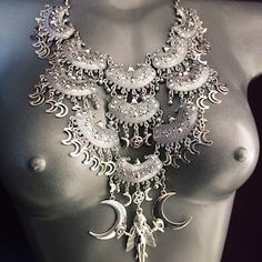 a white mannequin with silver jewelry on it's neck and two moon pendants hanging from the chest