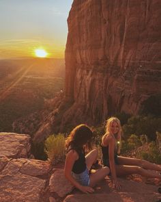 two young women sitting on the edge of a cliff at sunset, with mountains in the background