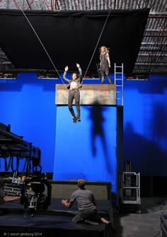 two people are suspended from the ceiling by ropes in an empty stage with blue walls