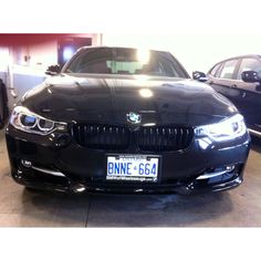 a black car parked in a garage next to two other bmws and one is missing the license plate