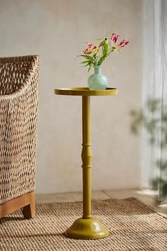 a small table with a vase on it and a wicker chair in the background