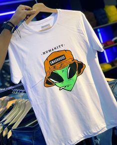 a person holding up a white shirt with an image of a green alien on it