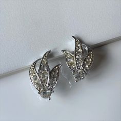 "Vintage mid century rhinestone clip on earrings, signed Sarah Coventry.  The design is known as \"Enchantress\" . Ornate shiny silver tone fan or leaf shaped earrings, with 11 clear round rhinestones. They are in very good condition and are signed on the back. Measurements: Approximately 1 1/8\" H x 3/4\" W at the widest point Condition: Very good condition overall, with no missing rhinestones and minimal wear on the back of the earrings.  Markings: The backs are signed \"SARAH COV\" for Sarah Wedding Earrings Vintage, Crystal Statement Earrings, Glam Earrings, Vintage Rhinestone Jewelry, Fall Earrings, Sarah Coventry, Pretty Necklaces, 925 Silver Earrings, Rhinestone Jewelry