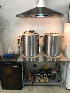 two large stainless steel pots sitting on top of a metal shelf next to a refrigerator