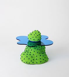 a green and blue object with black dots on it's body, sitting in front of a white background