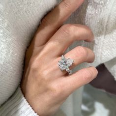 a woman's hand with a diamond ring on her finger, wearing a white sweater