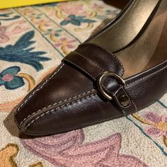 These Gorgeous Joan & David Dark Brown Leather Pumps Have Exquisite Contrast Stitching And A Fun Buckle Detail On The Toe- It Hints At A Sensible Loafer But The Eye Follows The Stitching To The Sexy Curvy Heel. They Have J&D Circa365 Technology Inside So They Are Beautiful And Comfortable! With A Glint Of Woodtone At The Heel- They’ll Look Great With A Sexy Dress For A Night On The Town Or With Jeans For Fall... Never Worn! Genuine Leather 3 Inch Heel Made In Italy For An American-Owned Company Classic Leather Court Shoes With Buckle Closure, Formal Brown Faux Leather Heels, Leather Closed Toe Court Shoes With Buckle, Leather Court Shoes With Buckle Closure, Leather Court Shoes With Buckle For Office, Leather Court Shoes With Buckle Closure For Office, Chic Brown Leather Court Shoes, Elegant Leather Court Shoes With Buckle Closure, Classic Leather Court Shoes With Heel Tab