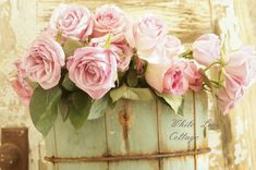 some pink roses are in a bucket on a table next to an old wooden door