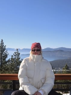 a woman sitting on top of a wooden bench next to a forest filled with trees