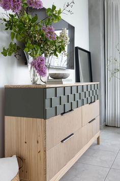 a vase filled with purple flowers sitting on top of a wooden dresser next to a mirror