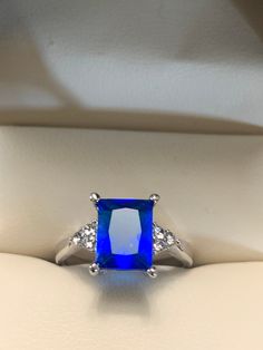 Dazzling blue is a bright color of blue and also the shade of this crystal ring.  This ring has an 8 x 10 mm emerald cut blue crystal on a silver band. The ring is a size 6.5 and is in excellent condition.  I could not find any scratches on the crystal or band.  The large blue crystal has 3 tiny bright crystals on each side. This is a perfect cocktail ring for someone who likes simplicity. Blue Sapphire Emerald Cut Jewelry, Blue Emerald Cut Sapphire Jewelry, Emerald Cut Sapphire Blue Jewelry, Emerald Cut Blue Sapphire Jewelry, Blue Emerald-cut Sapphire Ring In Sterling Silver, Blue Sapphire Ring In Emerald Cut Sterling Silver, Blue Square Cut Sapphire Jewelry, Blue Emerald Cut Jewelry Gift, Blue Sapphire Emerald Cut Promise Ring