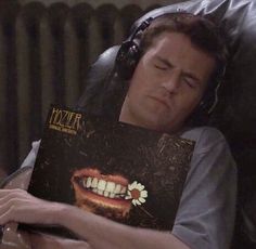 a man laying in a chair with a book on his lap and headphones around his neck